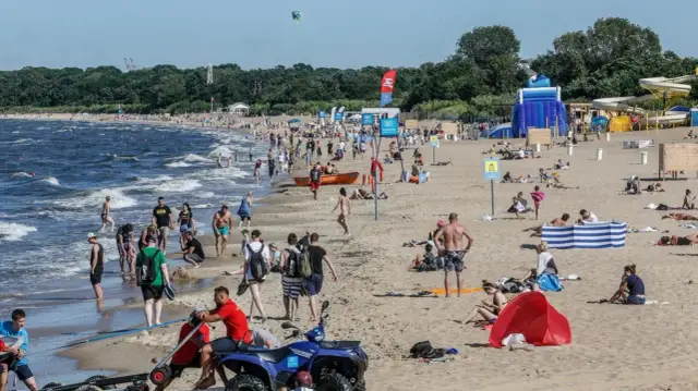 Tłum ludzi na piaszczystej plaży nad Bałtykiem w słoneczny dzień.