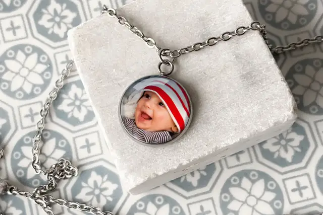 Srebrny wisiorek z okrągłym zdjęciem uśmiechniętego dziecka w czapce w paski.