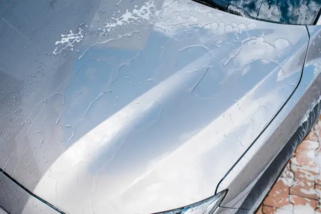 Krople wody i piany na masce srebrnego auta. Czy po woskowaniu auto trzeba płukać?
