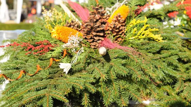 Podłużny stroik cmentarny z gałązek iglastych, szyszek i ozdób.