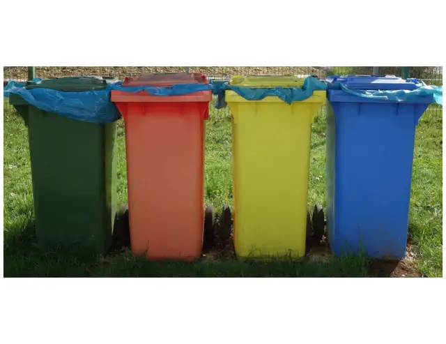 Cztery kolorowe kosze na śmieci stojące obok siebie na trawie.