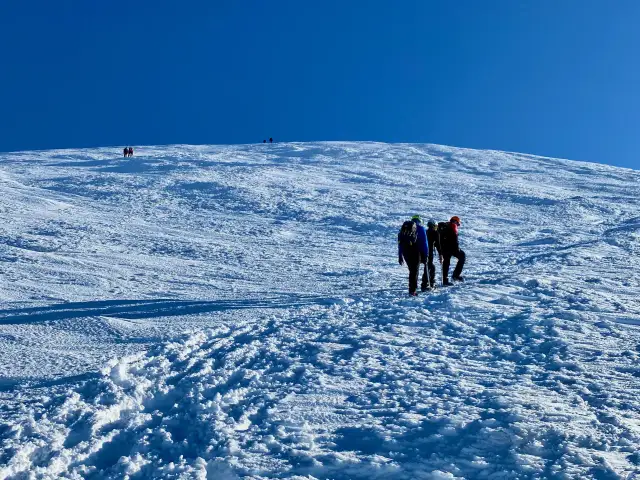 Grupa turystów wspina się po ośnieżonym zboczu. W oddali widać kolejne osoby. To piękny dzień na zdobywanie czerwonych wierchów Białki.