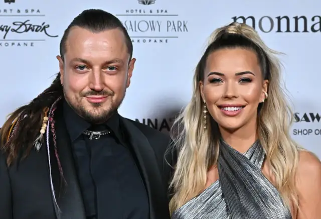 Baron z żoną, uśmiechnięci, pozują do zdjęcia. On ma warkocze, ona błyszczącą sukienkę.