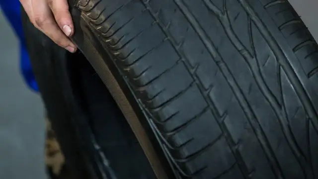 Dłoń pokazuje zużytą oponę samochodową z widocznym bieżnikiem.