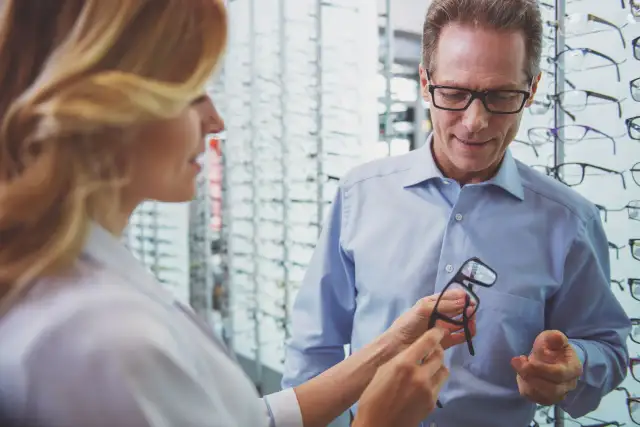 Kobieta w okularach pokazuje mężczyźnie okulary w salonie optycznym.