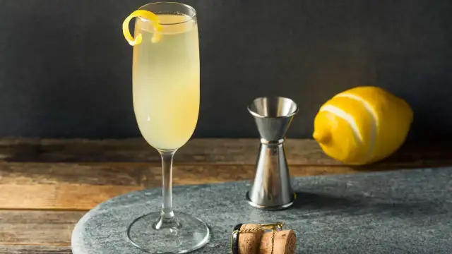 French 75 na ginie kontra French 75 na koniaku. Elegancki drink z cytrynową skórką, kieliszek, miarka barmańska, cytryna i korek od szampana.