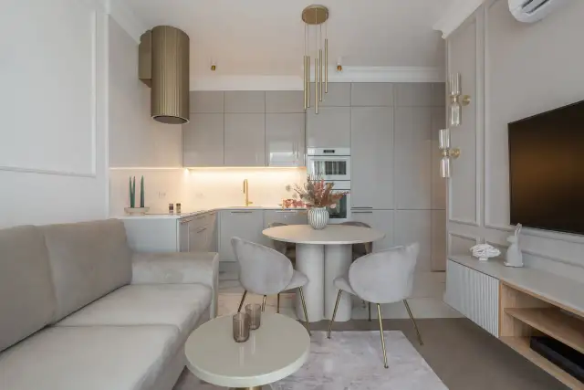 Nowoczesny projekt mieszkania 45m2: salon z beżową kanapą, okrągły stół z krzesłami, kuchnia z szarymi frontami i złoty okap.