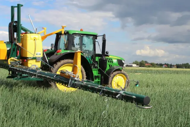 Zielony traktor z opryskiwaczem na polu. Warto sprawdzić movento 100 sc dawkowanie dla optymalnych rezultatów.