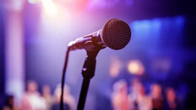 Mikrofon na scenie, gotowy na występ Karola Modzelewskiego. W tle rozmyta publiczność i światła.