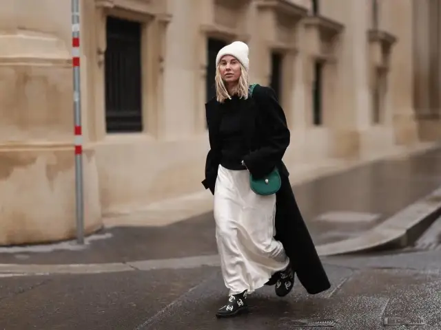 Kobieta w białej spódnicy i czarnym płaszczu, z zieloną torebką. Idealna stylizacja: jaka bluzka do białej spódnicy?