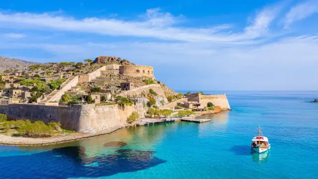 Piękna pogoda w Grecji. Fortyfikacje Spinalongi na tle błękitnego morza i nieba. Mała łódź kołysze się na falach.