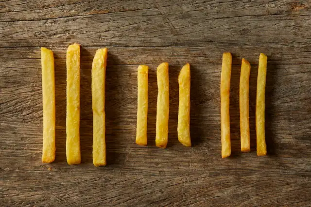 Kilka złotych frytek ułożonych w rzędach na drewnianym tle.