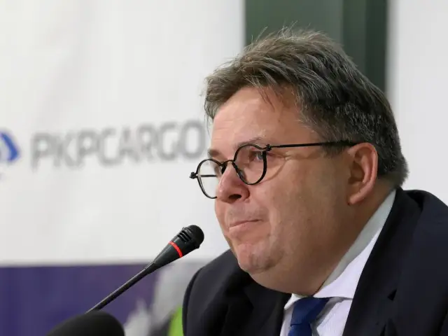 Mężczyzna w okularach przed mikrofonem na tle logo PKP Cargo.