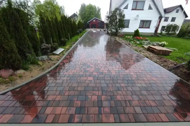 Mokry podjazd z kostki brukowej w odcieniach czerwieni i brązu, prowadzący do domu.