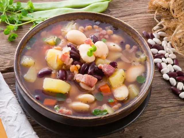Miseczka sycącej zupy fasolowej z ziemniakami, boczkiem i różnymi rodzajami fasoli.