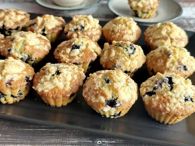 Muffinki z jagodami i kruszonką na ciemnej tacy.