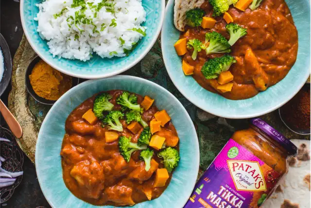 Dwa talerze z indyjskim curry z dynią i brokułami, ryżem i słoikiem sosu Tikka Masala.