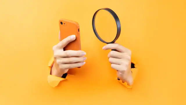 Ręce trzymające pomarańczowy iPhone i lupę, sugerujące, jak namierzyć iPhone po IMEI.