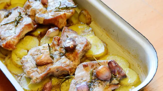 Pieczona karkówka z ziemniakami, czosnkiem i rozmarynem w naczyniu żaroodpornym.
