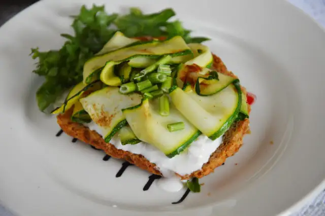 Kanapka z cukinią, serem i sałatą na białym talerzu.