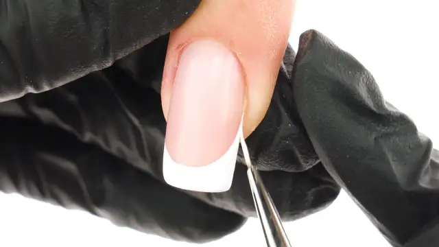 Precyzyjne malowanie białej końcówki french manicure bez użycia pasków. Dłoń w czarnej rękawiczce trzyma pędzelek.