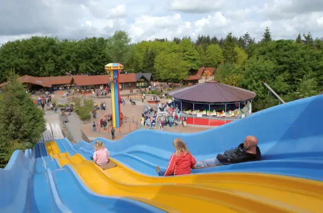 Familienrutsche im Tolk-Schau Freizeitpark mit Menschen, die rutschen und Karussell.