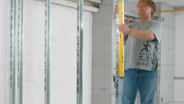 Mężczyzna z poziomicą sprawdza pionowe profile, przygotowując się do montażu półek z karton gipsu.