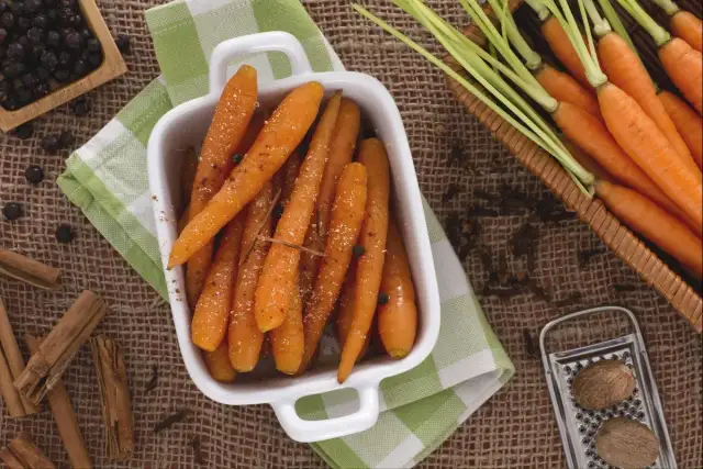 Carottes rôties dans un plat blanc, entourées d'épices : cannelle, genièvre, noix de muscade.