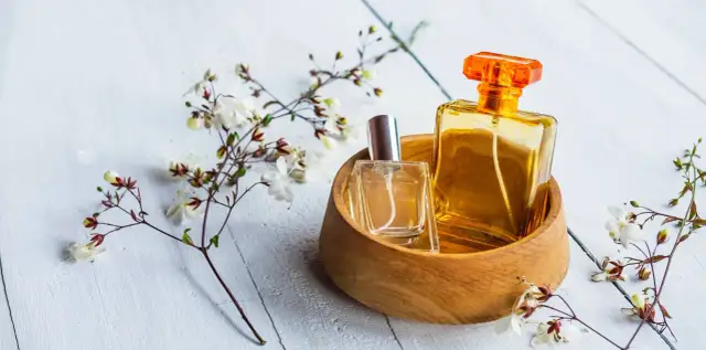 Dwie buteleczki perfum, jedna w szkle, druga w bursztynowym kolorze, w drewnianej miseczce, otoczone delikatnymi kwiatami. Czy to woda toaletowa czy tester?