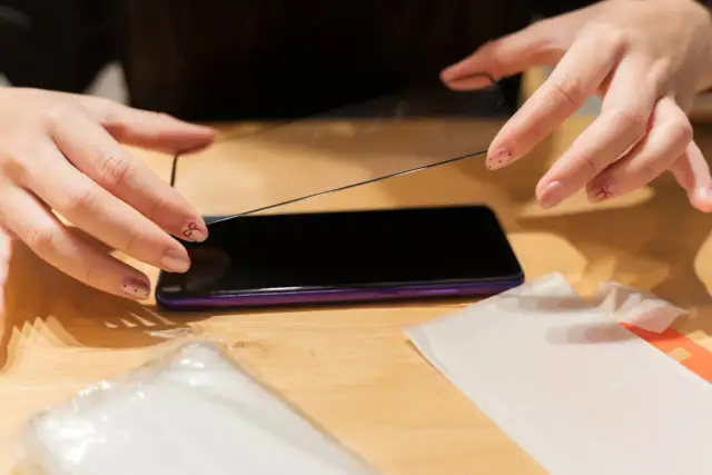 Dłonie przygotowują się do nałożenia szkła hydrożelowego na ekran telefonu.