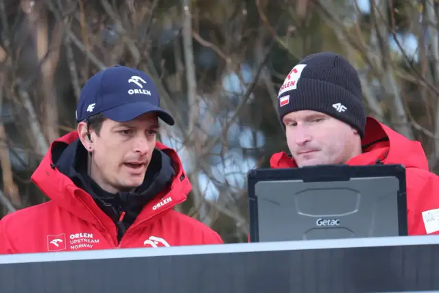 Dwóch trenerów w czerwonych kurtkach Orlen analizuje dane na tablecie. To oni decydują, kto trenuje polskich skoczków.