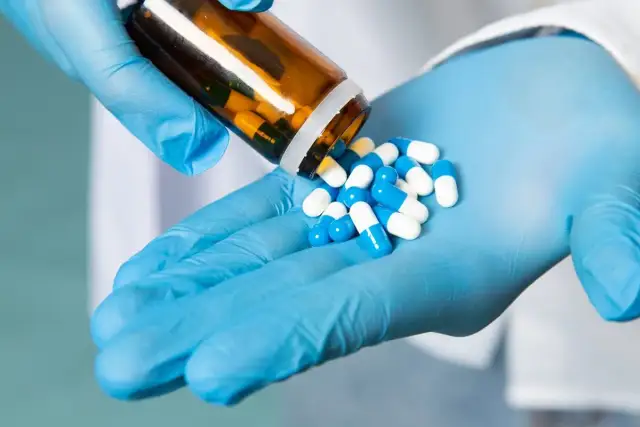 Rękawiczki chirurgiczne i buteleczka z lekami. W stomatologii antybiotyki są często przepisywane, aby zapobiegać infekcjom.