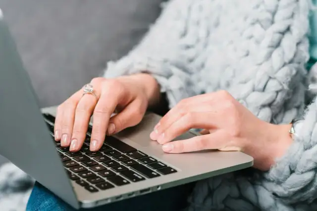 Kobieta w ciepłym swetrze uczy się, jak kupić obligacje skarbowe, wpisując dane na laptopie.