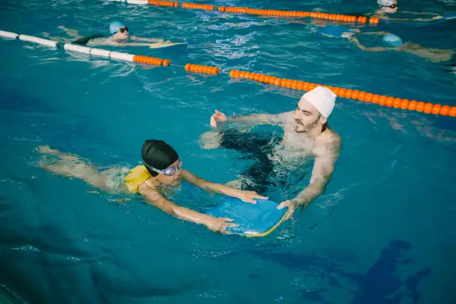 Instruktor pływania pomaga dziecku z deską w basenie.