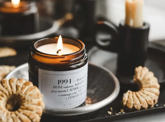 Płonąca świeca zapachowa w szklanym słoiku, obok ciasteczka i inne świece.