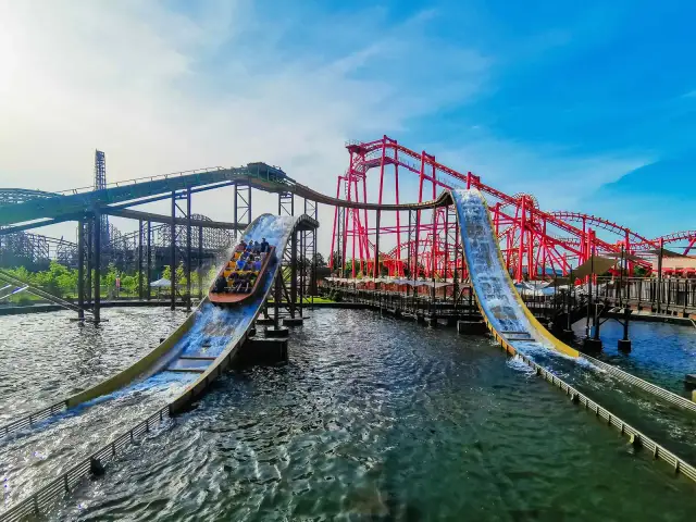 Energylandia Zator atrakcje: łodzie z pasażerami zjeżdżają po stromych zjeżdżalniach wodnych, w tle czerwone rollercoastery.