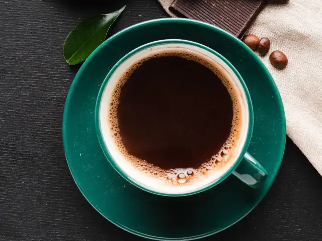 Aromatic coffee in a green cup, next to chocolate and beans. Czy kawa podnosi kortyzol? This morning brew might be the answer.