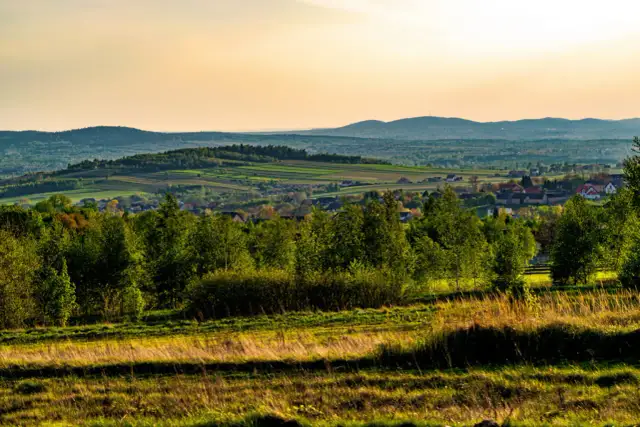 Krajobraz Gór Świętokrzyskich z pagórkami, polami i lasami w ciepłym świetle zachodzącego słońca.