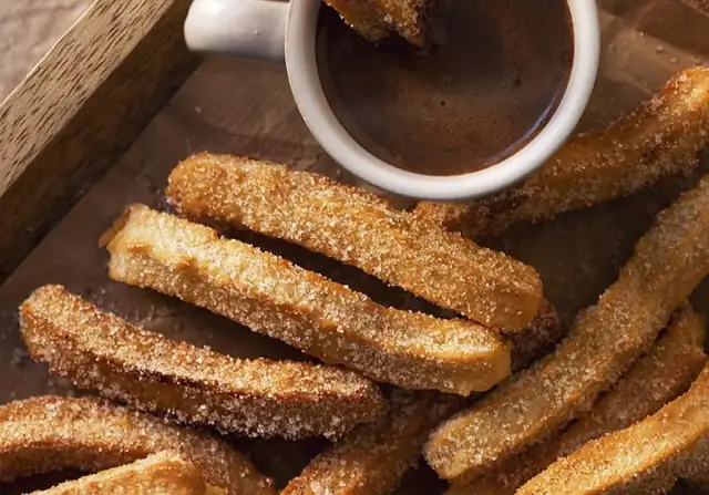 Churros caseros espolvoreados con azúcar junto a una taza de chocolate caliente.