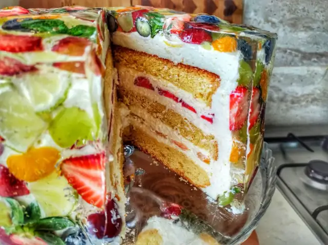 Kolorowy tort z galaretką i owocami, przekrojony, ukazujący warstwy biszkoptu i kremu.