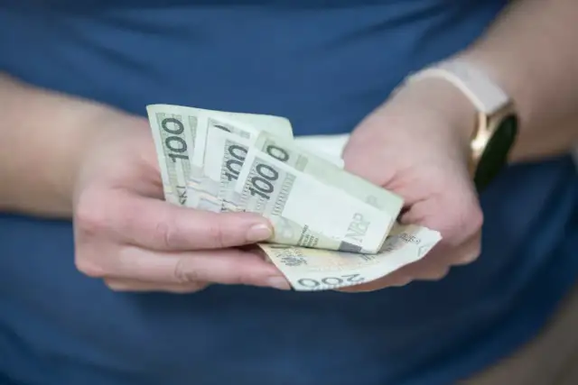 Dłonie trzymające banknoty 100 zł i 200 zł. Zastanawiasz się, o ile wzrośnie oprocentowanie lokat?