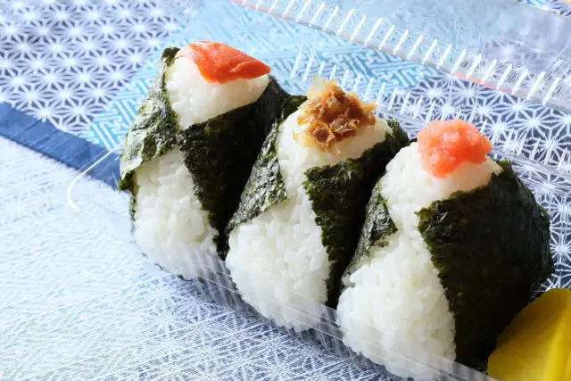 Trzy onigiri z ryżem, zawinięte w nori, z łososiem, tuńczykiem i ikrą na wierzchu. Idealne na przekąskę.