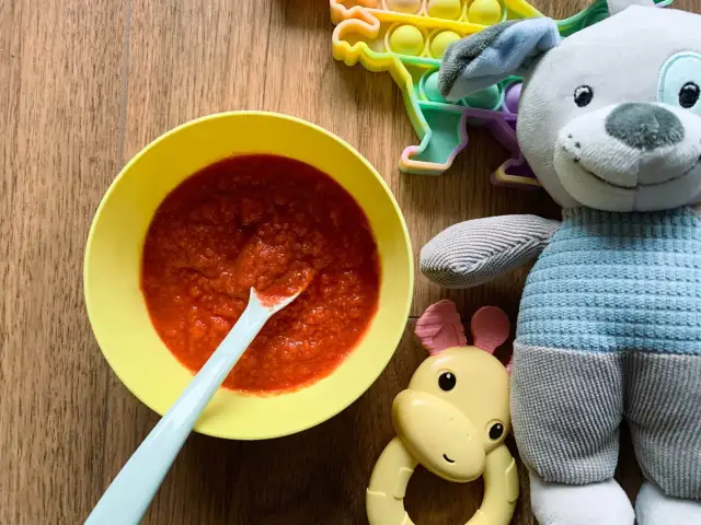 Pyszna zupa buraczkowa dla niemowlaka w żółtej miseczce, obok pluszowy piesek i gryzak.