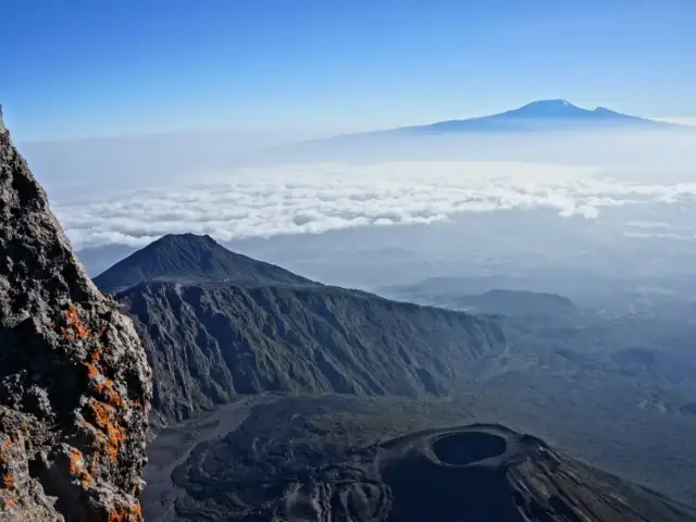 Widok z góry na wulkaniczne krajobrazy. Czy Kilimandżaro to trudno wejść? Widoczne inne szczyty i morze chmur.