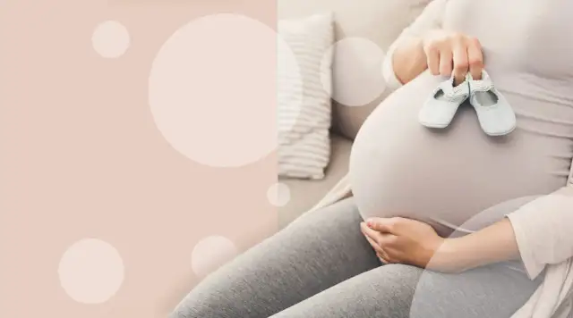 Ciężarna kobieta trzymająca małe buciki na brzuchu.