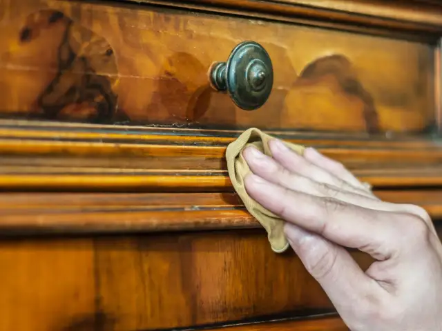 Dłoń czyści drewniany mebel. Zastanawiasz się, czym pomalować fornir, by nadać mu nowy wygląd?