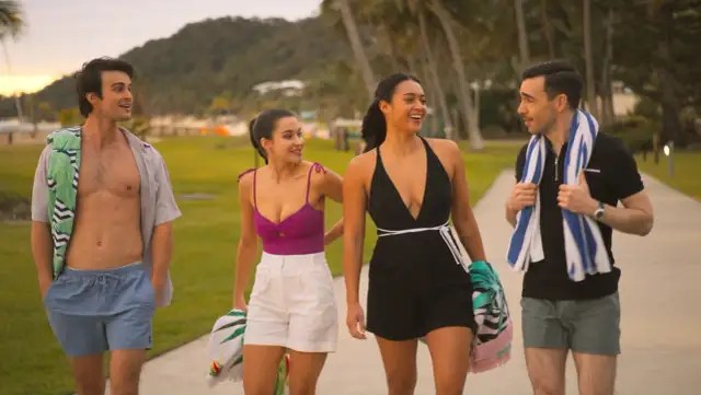 Para idzie plażą, czując miłość na rajskich wyspach. Słońce zachodzi, tworząc ciepłą atmosferę.