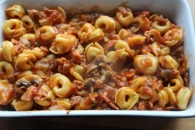 Tortellini z mięsem w sosie pomidorowym z grzybami i boczkiem w naczyniu żaroodpornym.