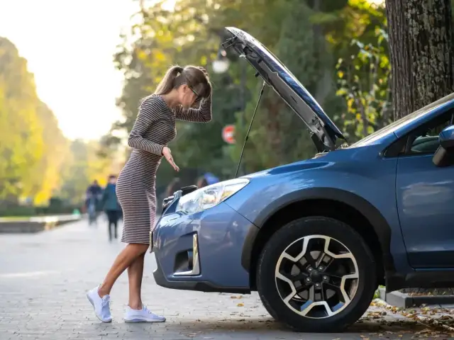 Kobieta zmartwiona patrzy pod maskę auta, szukając przyczyn problemów. Czy to objawy awarii pompy paliwa?