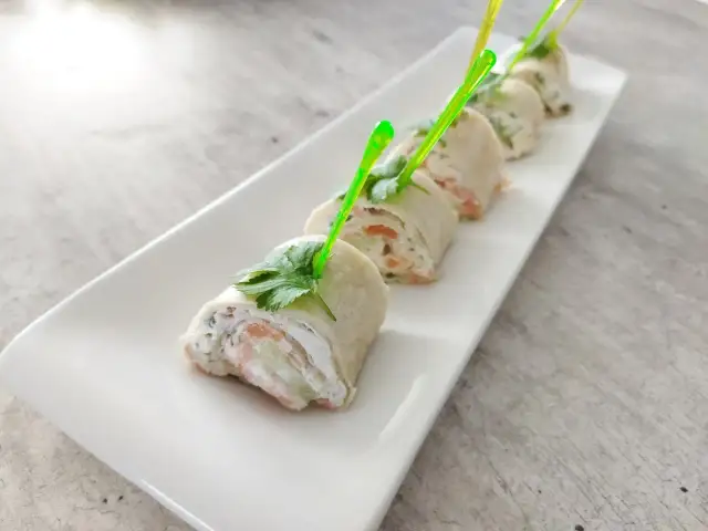 Roladki z tortilli z łososiem, kremowym serkiem i ogórkiem, udekorowane natką pietruszki. Idealne na przekąskę.